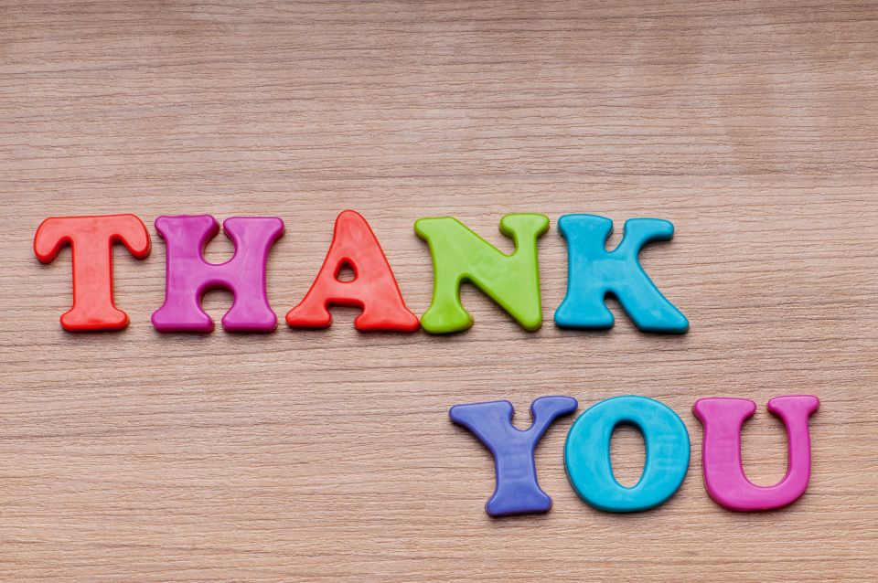 Thank You spelled out with child's magnetic letters on wood grain background.