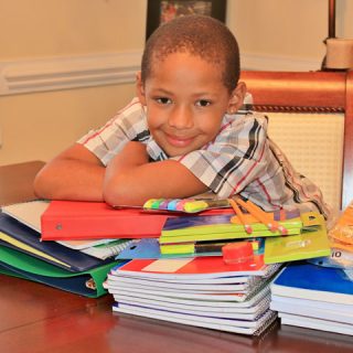 Boy leaning over a stack of school supplies with a grin on his face.